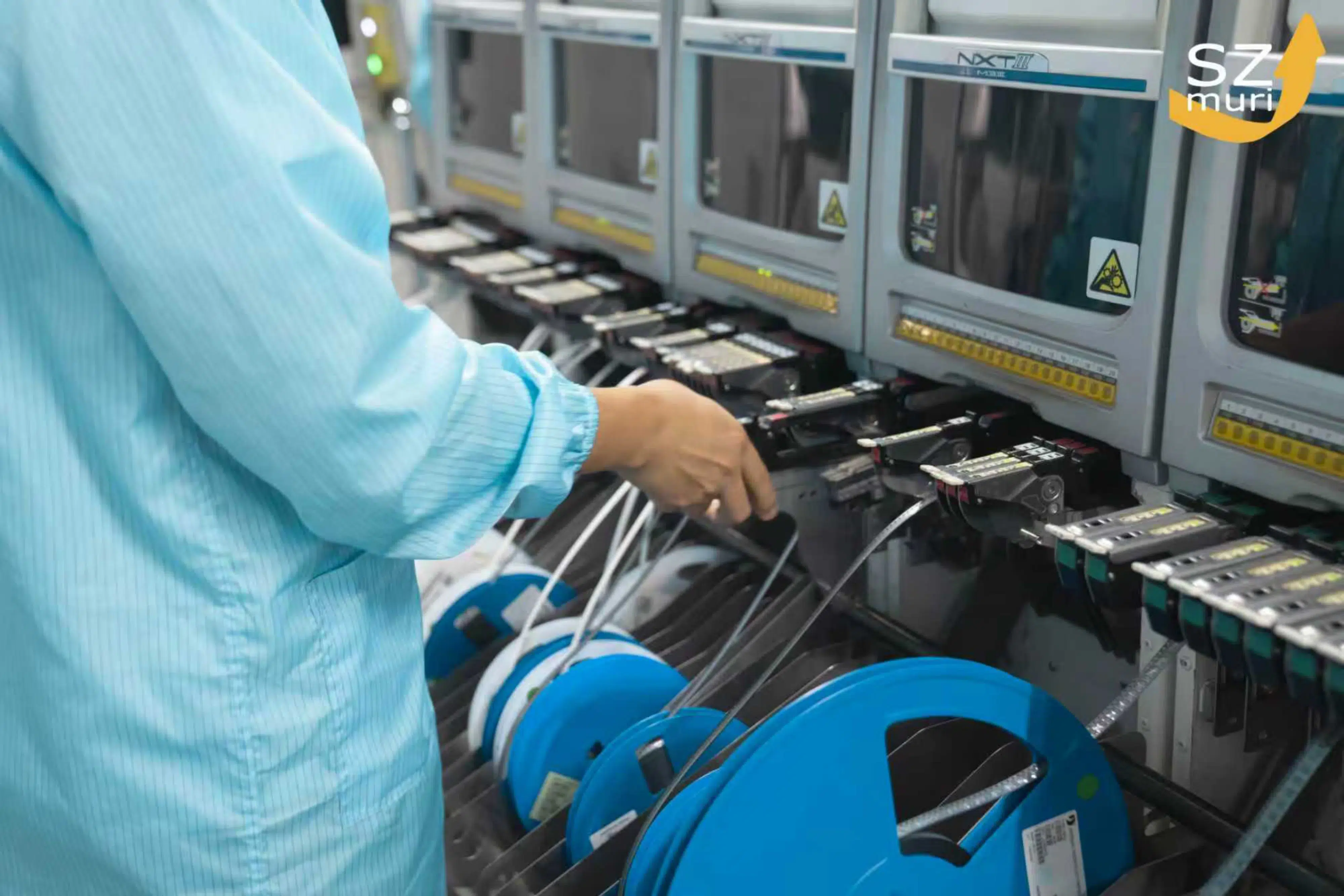 Eine Person in blauer Arbeitskleidung bedient Maschinen mit blauen Kabeltrommeln