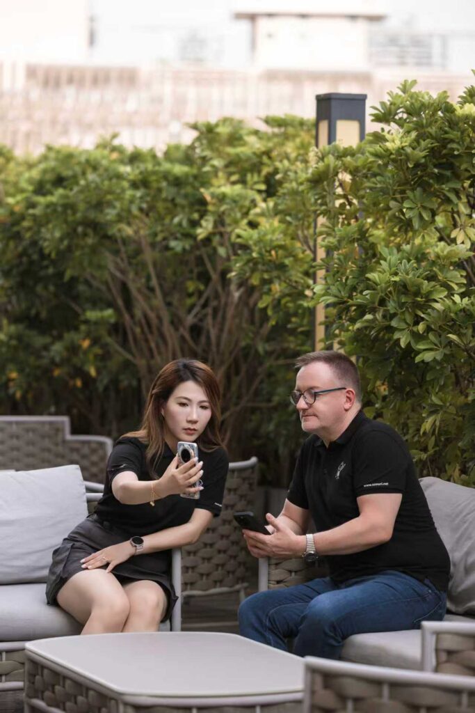 Zwei Personen sitzen draußen auf Sofas, sie schauen gemeinsam auf ein Smartphone