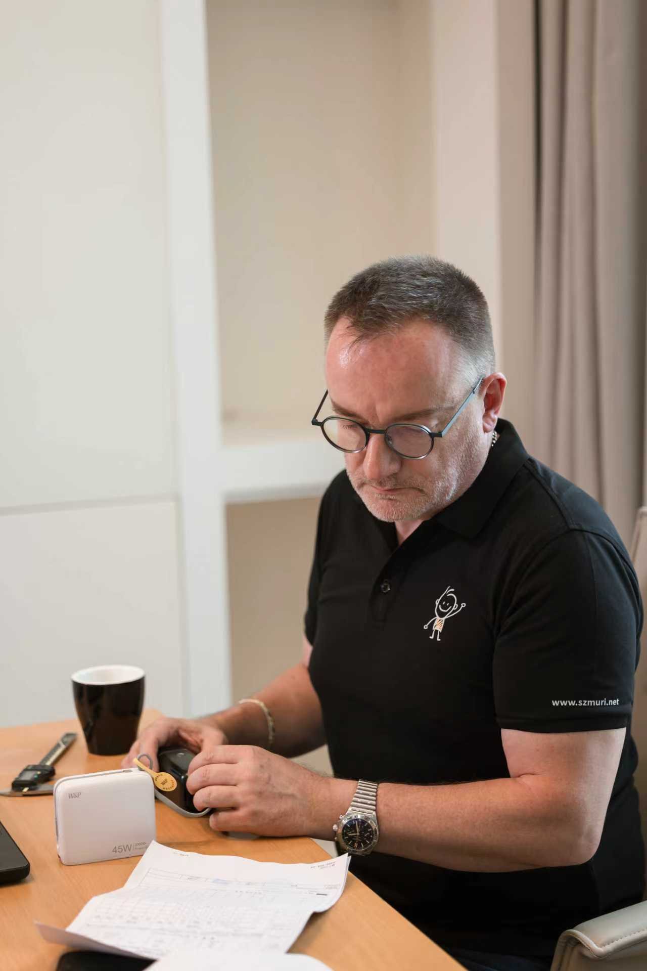 Ein Mann mit Brille sitzt konzentriert am Schreibtisch und prüft ein Messgerät